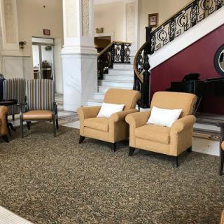 A cozy hotel lobby with armchairs, a grand staircase, and a piano.