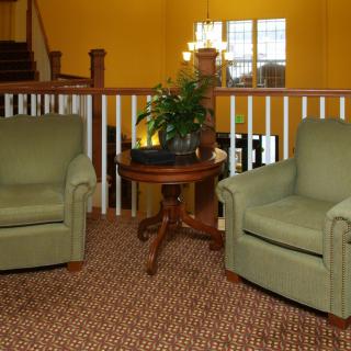 A cozy living room setup featuring two green armchairs and a wooden table with a plant, set against a warm yellow background.