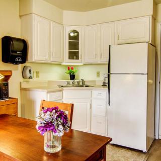 A cozy kitchen with white cabinets, a dining table adorned with flowers, and a refrigerator.