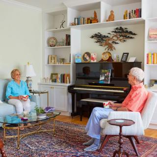 Two elderly individuals sitting in a cozy living room, engaged in conversation near a piano.