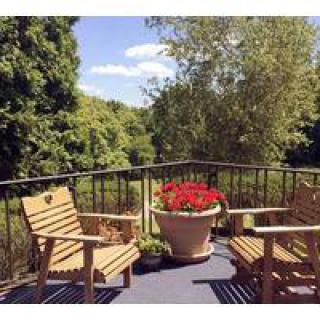 A peaceful patio setting with wooden chairs and a flower pot, surrounded by lush greenery.