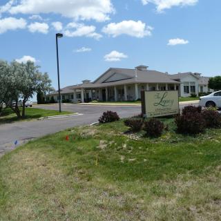 A building with a sign in front, surrounded by grass and a clear sky with clouds.