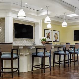 A modern bar area with high chairs, pendant lighting, and a large television.