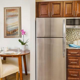 A modern kitchen with wooden cabinetry and stainless steel appliances, featuring a cozy dining area with an orchid plant and wall art.