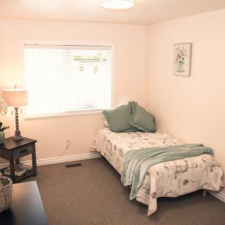 A minimalist bedroom featuring a single bed, a lamp, and a window providing natural light.
