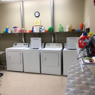 A laundry room with washing machines, dryers, and shelves stocked with detergent bottles.