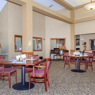 An empty dining room with arranged tables and chairs, featuring a carpeted floor and high ceilings.