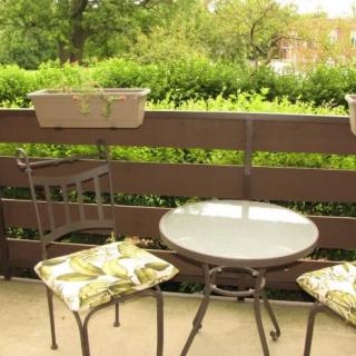 A cozy balcony with a small round table and two cushioned chairs, surrounded by greenery.