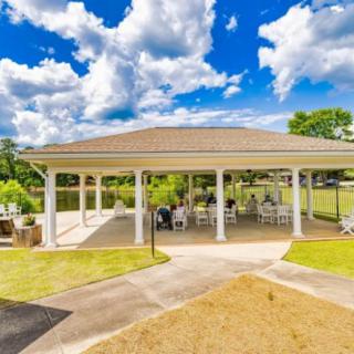 An outdoor pavilion with seating, set against a backdrop of lush greenery and a partly cloudy sky.