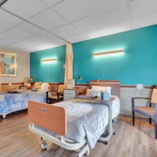 A hospital room with two beds, teal-colored walls, and medical equipment.