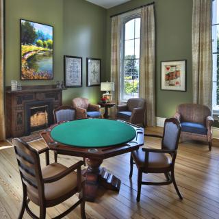 A classic room with a poker table surrounded by chairs, featuring green walls and framed artwork.