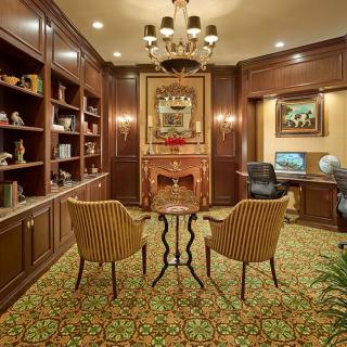 A cozy library room with elegant wood paneling, featuring bookshelves, a decorative fireplace, and comfortable seating.