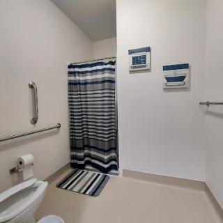 A spacious and modern bathroom featuring a striped shower curtain, matching bath mat, and accessibility features.