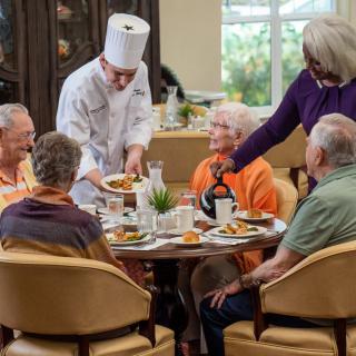 A group of elderly people enjoying a meal together as a chef serves food at their table.