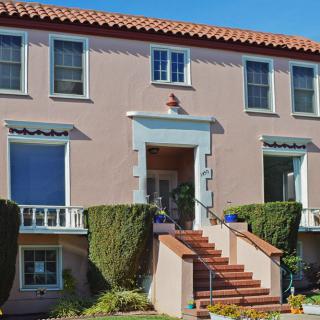 A two-story residential house with a tiled roof and manicured shrubs lining the entrance steps.