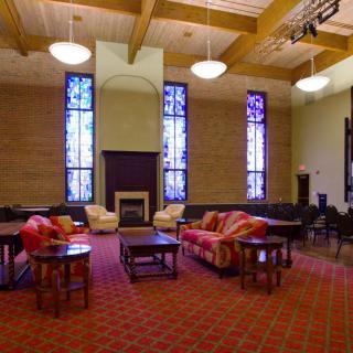 A spacious room with comfortable seating, featuring stained glass windows and a fireplace.