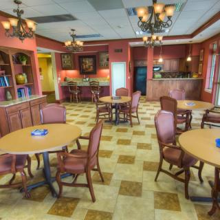 A cozy dining area with several round tables and upholstered chairs, illuminated by elegant chandeliers.
