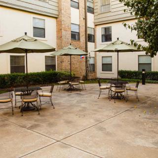 A courtyard with tables and umbrellas, surrounded by a multi-story building.