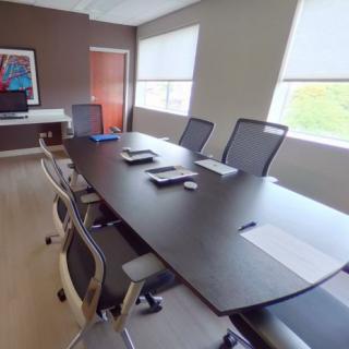 A modern conference room with a long table, chairs, and large windows.