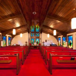 Interior view of a church with red carpet, wooden ceiling, and stained glass windows.