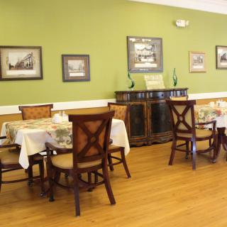 A cozy dining room with wooden furniture and green walls, featuring framed pictures and a sideboard.