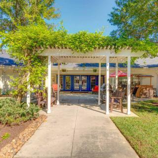 A sunny entrance to a building with a pergola and surrounding greenery.