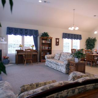 A cozy living room with a floral sofa and wooden furniture, featuring large windows and a dining area.