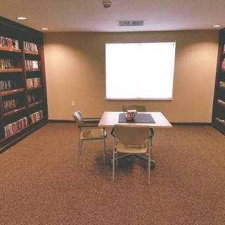 A quiet library reading room with bookshelves, a table, and chairs.
