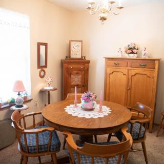 A cozy dining room with a round wooden table and matching chairs, adorned with decorative items and natural light.