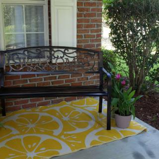 A cozy porch with a metal bench, lemon-patterned rug, and a potted plant.