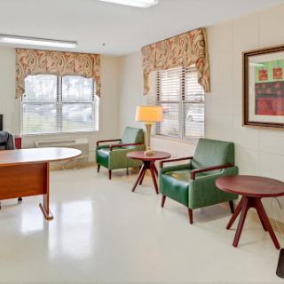 A cozy waiting area featuring comfortable green chairs, a wooden table, and decorative art on the wall.