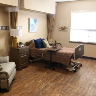 A well-furnished hospital room featuring a single bed, chair, and natural light from a window.