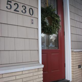 A house with a red door adorned with a wreath and the address number 5230.