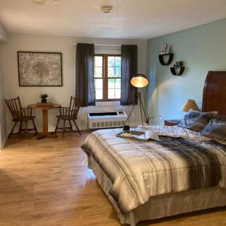 A cozy bedroom with a wooden floor, featuring a comfortable bed, a small sitting area with chairs, and soft lighting.