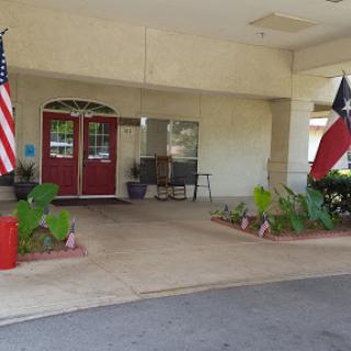 The welcoming entrance of a building adorned with American and Texas flags, surrounded by lush landscaping.