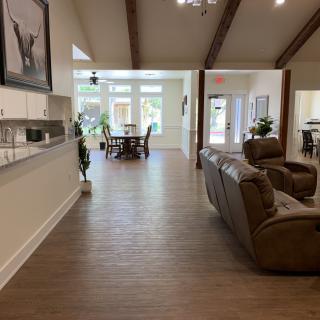 A modern open-concept living room with a view of the dining area, featuring wooden floors and natural light.