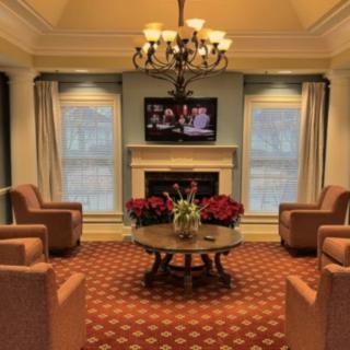 A cozy living room with armchairs, a chandelier, and a fireplace beneath a mounted television.