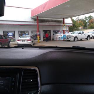 A view of a gas station from the inside of a vehicle, showing parked cars and the storefront.
