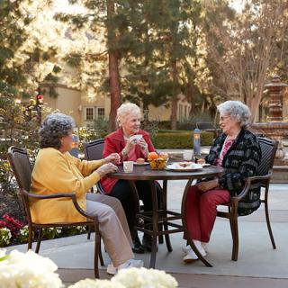 Three elderly women enjoying a conversation outdoors on a patio.