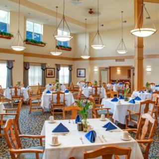 A well-arranged dining area with tables set for service, featuring wooden chairs and elegant lighting.