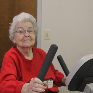 An elderly woman exercising on a stationary bike, promoting health and fitness.