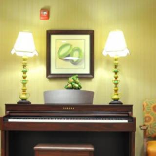 A cozy interior featuring a piano with two decorative lamps and artwork above.