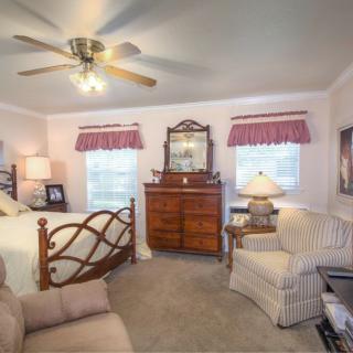 A cozy bedroom with a bed, dresser, chair, and ceiling fan.