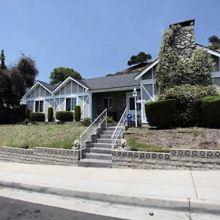 A residential house with a stone chimney and landscaped front yard during the daytime.