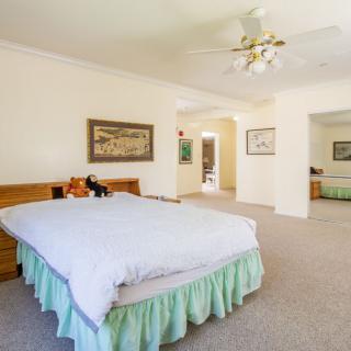 A spacious bedroom with a large bed, ceiling fan, and carpeted floor.