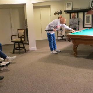 A person playing billiards while others watch in a cozy indoor setting.