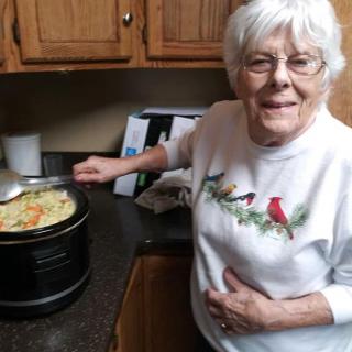 Elderly woman cooking in the kitchen, smiling at the camera.
