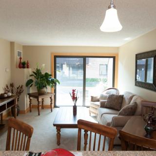A cozy living room with a seating area, coffee table, dining chairs, and a large window providing natural light.