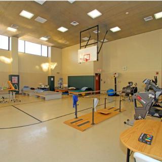 An indoor gym with a basketball hoop and various exercise equipment for rehabilitation and fitness activities.
