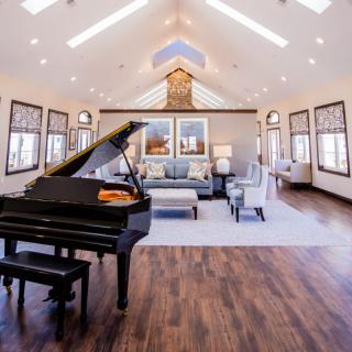 A luxurious and spacious living room featuring a grand piano, hardwood floors, and ample natural light.